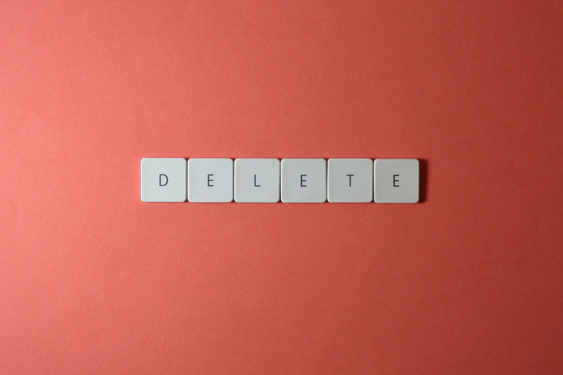 Six white keyboard keys, each with a black letter, spell out “DELETE” in a row on a plain coral red background—a fitting image for an Office Manager ready to delete voicemail and keep things organized.