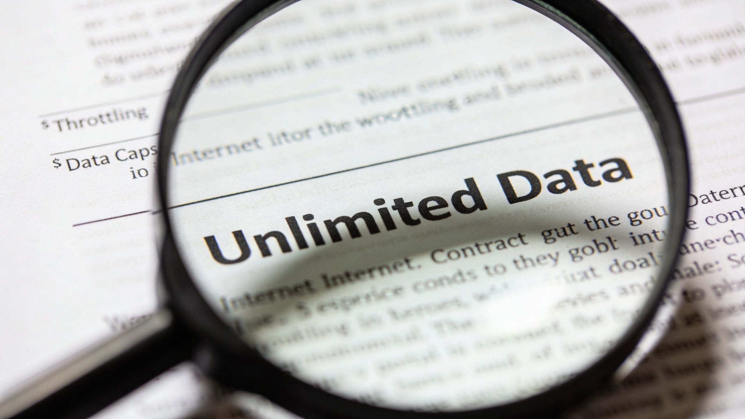 A magnifying glass focusing on the words Unlimited Data printed on a paper document.